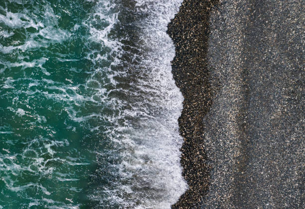 istock Green sea waves break on black sand and pebbles shore, aerial texture 1338467378