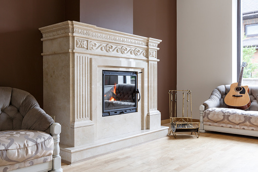 White marble fireplace in classic style with burning wood inside. Interior design concept