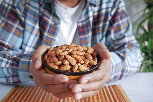 young man hand hold a bowl of almond nut white sited ,