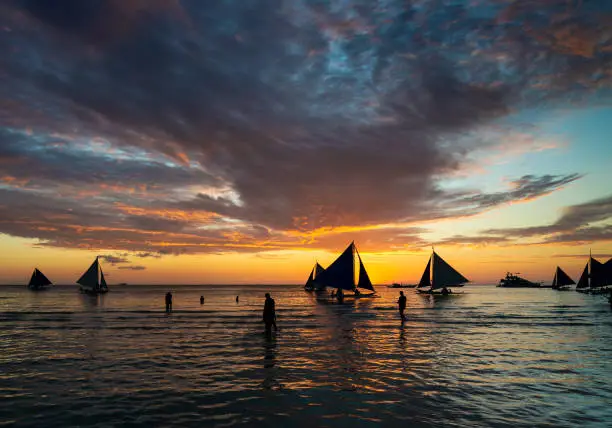 Photo of beautiful tropical sunset with sailing boats and tourists in boracay island beach philippines