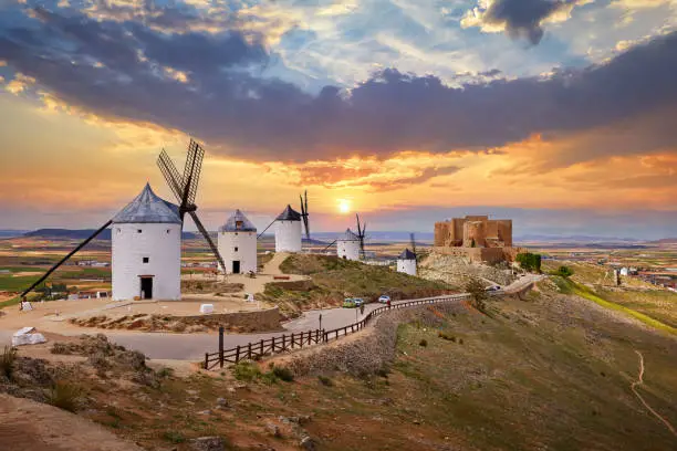 Wind mills and old castle in Consuegra, Toledo, Castilla La Mancha, Spain. Picturesque panorama landscape with road and view to ancient walls and windmills on blue sky with clouds.