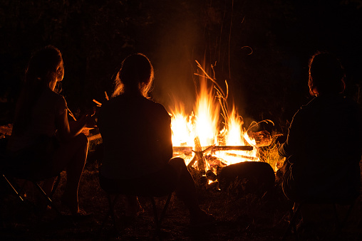 Tourism and rest. Silhouettes of people in the dark on the background of a campfire with sparks. Communication and friendship.
