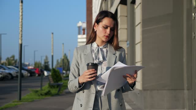 young woman in a business suit with coffee and documents walking down the street