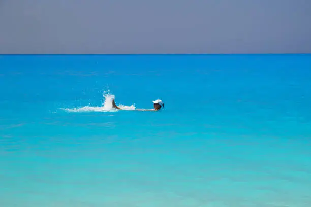 Photo of Young woman in white cap swimming in fantastic turquoise and blue Ionian Sea water at Myrtos Beach in Greece