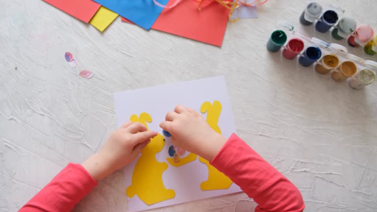 Child making card with Easter bunnies  from colorful paper. Applique. Handmade. Project of children's creativity, handicrafts, crafts for kids.