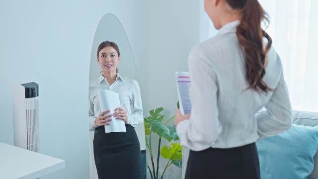 Asian applicant prepare for job interview in front of mirror at home. Attractive beautiful female feel nervous and excited while waiting for apply job with hr manager and practice speak with resume.