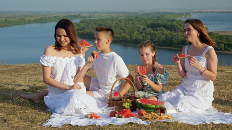 Positive lady with daughters and son on riverbank at picnic