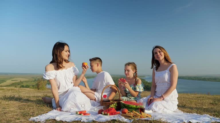 Positive lady with daughters and son on riverbank at picnic