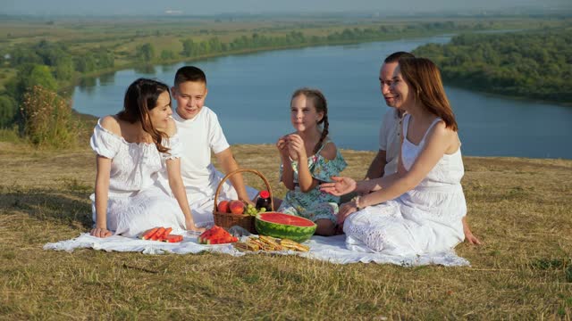 Happy family with children has picnic on hilly riverbank