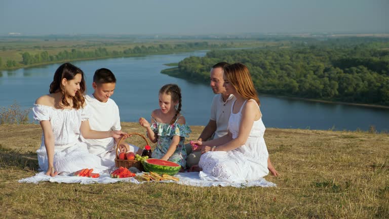 Happy family with children has picnic on hilly riverbank