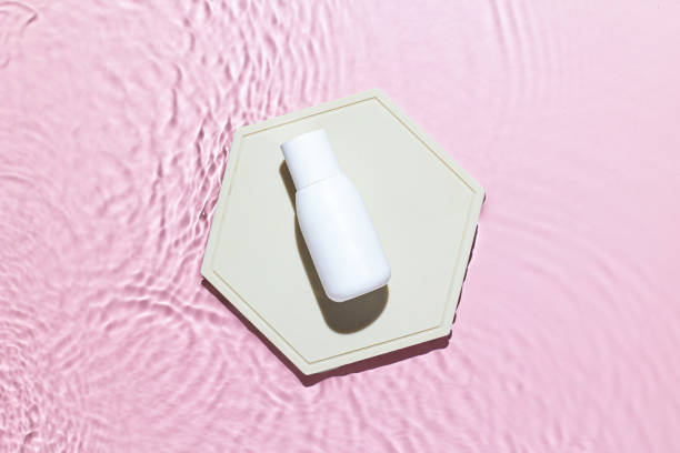 istock Pink water texture surface with white bottle on podium, ripples and transparent at sunlight. Backdrop for cosmetic or spa concept background. Copy space 1338488693