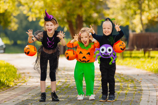 tre bambini con un cestino per dolci che fanno smorfie durante le vacanze di halloween all'aperto - trick or treat foto e immagini stock