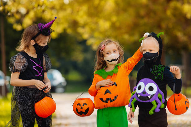 istock Three kid with a basket for sweets making grimaces wearing face mask on Halloween holiday 1338495438