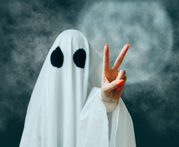 istock White ghost showing peace gesture in Halloween full moon night. 1338496643