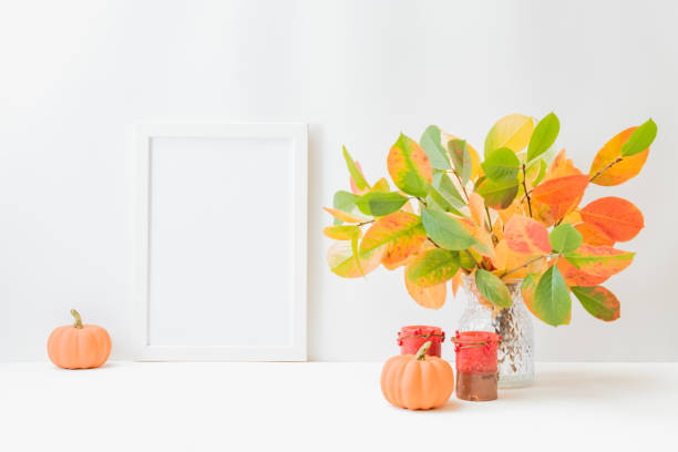 istock Home interior with decor elements. Mockup with a white frame, colorful autumn leaves in a vase on a light background 1338499972