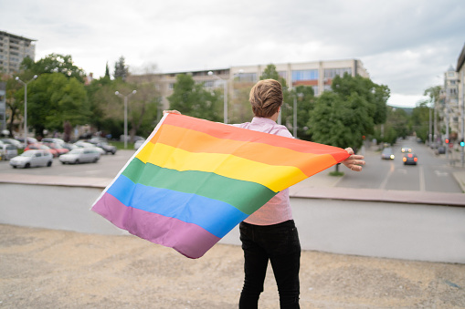 Young gay man, holding the rainbow flag behind his back