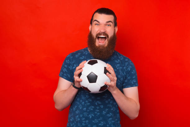 istock Screaming joyful bearded man is holding a soccer ball with both hands. 1338512986