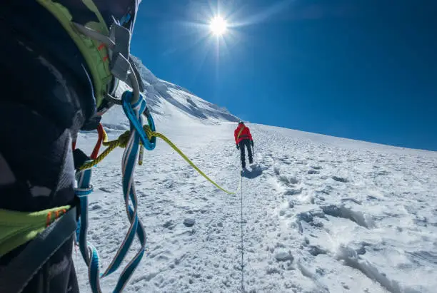 Rope team ascending Mont Blanc (Monte Bianco) summit 4,808m dressed red mountaineering clothes walking by snowy slopes with carabiner Climbing harness and green dynamic rope on the close up foreground
