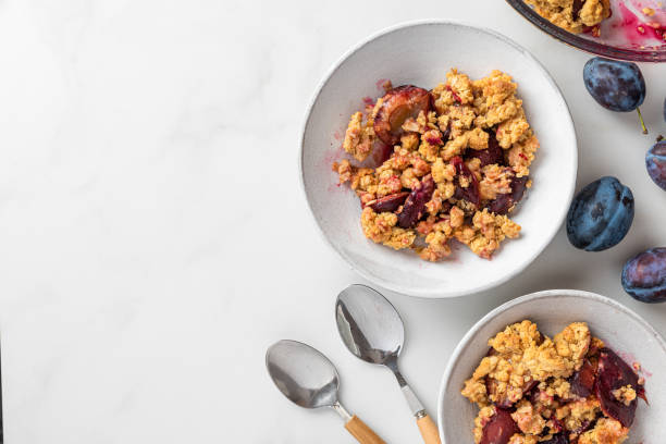 istock Fruit crumble. Plum crumble pie in plates with spoons on white marble table for tasty breakfast. Top view 1338515560