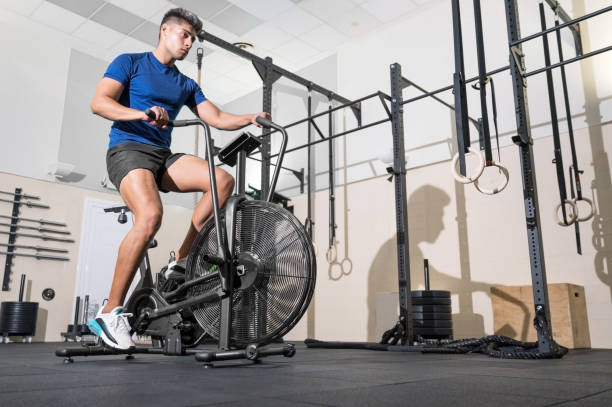 homem em forma fazendo treinamento cardio em máquina de bicicleta aérea estacionária com ventilador na academia. foto de alta qualidade - pedal bicycle sports training cycling - fotografias e filmes do acervo