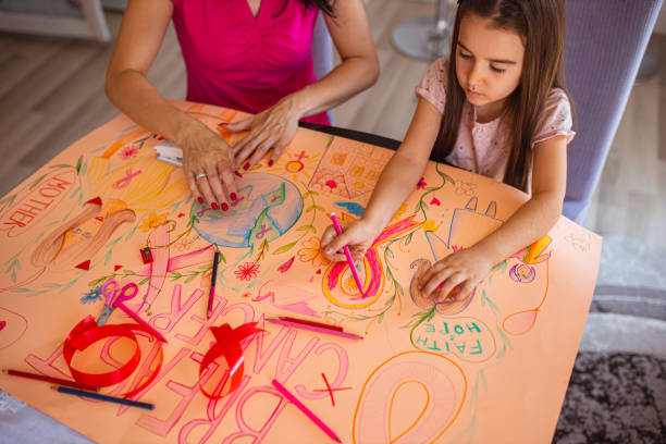 mutter unterrichtet ihre tochter über brustkrebsbewusstsein, während beide ein poster machen, um unterstützung zu zeigen - community outreach connection child paper stock-fotos und bilder