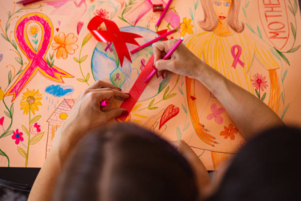 daughter helping her mother to make a poster and red ribbon, during month of breast cancer awareness - community outreach connection child paper imagens e fotografias de stock