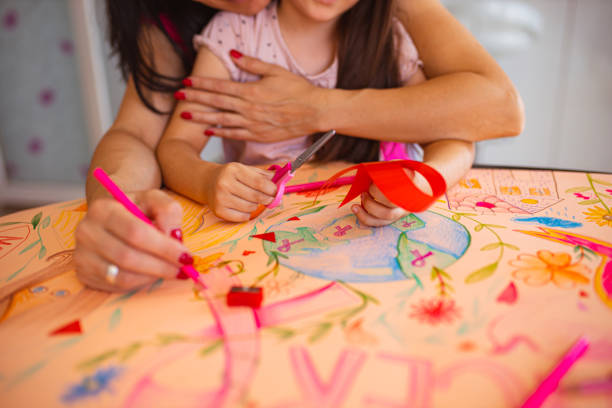 charmante tochter, die ihrer mutter, die brustkrebsüberlebende ist, hilft, ein poster für einen brustkrebsmonat zu machen - community outreach connection child paper stock-fotos und bilder