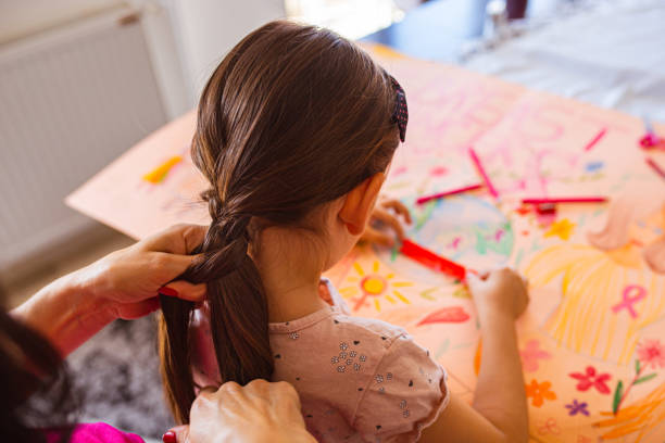 mother doing her daughter hair, while she making a breast cancer awareness poster - community outreach connection child paper imagens e fotografias de stock