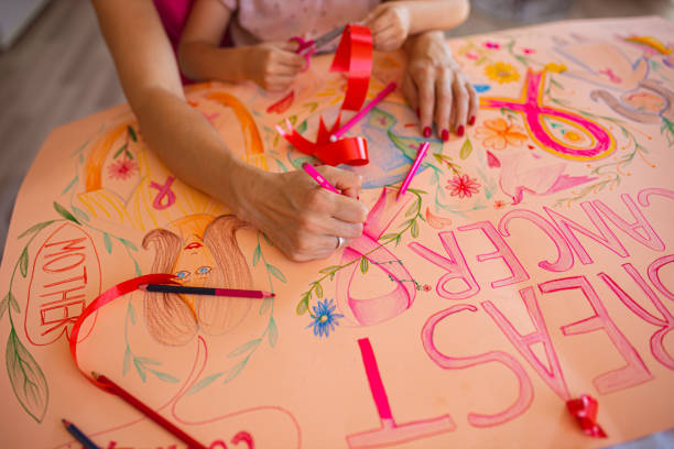 brustkrebsüberlebende und ihre tochter zeichnen ein brustbewusstseinsposter, um die gemeinschaft zu erreichen und allen frauen unterstützung zu zeigen - community outreach connection child paper stock-fotos und bilder