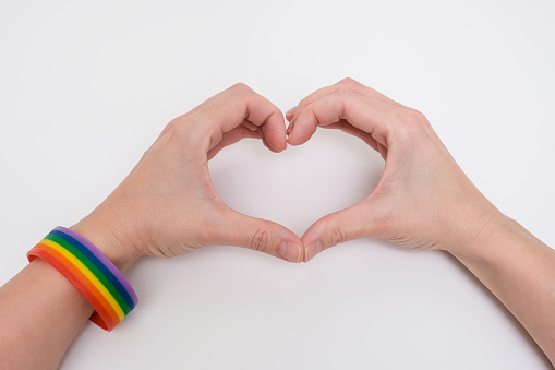 Hands wearing lgbtq rainbow bracelet folding a shape of a heart.
