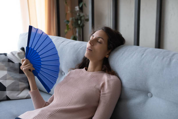 istock Overheated woman sit on sofa wave hand fan reduce heat 1338521581