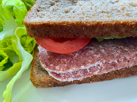 Stock photo showing a close-up view of corned beef sandwich with salad of green lettuce leaves and tomato slices. The sandwich has been made with a sliced wholemeal bread and is part of a healthy eating plan / diet.