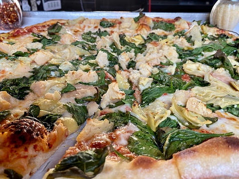 Large, whole New Haven style pizza, which is a thin crust, coal fired Neapolitan pie. The pizza is topped with spinach, artichoke hearts, and mashed potato.