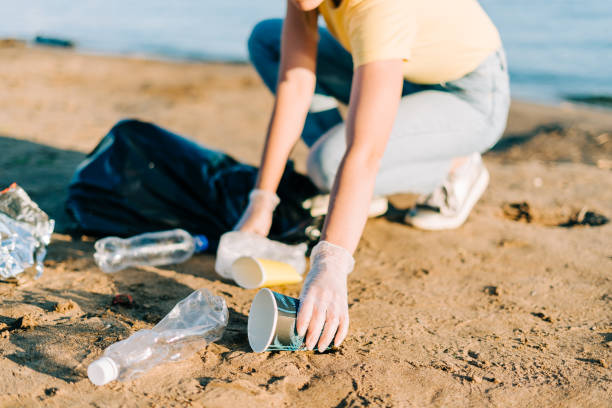 Young female volunteer hand satisfied with picking up trash, a plastic bottles and coffee cups, clean up beach with a sea. Woman collecting garbage. Environmental ecology pollution concept. Earth Day Young female volunteer hand satisfied with picking up trash, a plastic bottles and coffee cups, clean up beach with a sea. Woman collecting garbage. Environmental ecology pollution concept. Earth Day. littering stock pictures, royalty-free photos & images