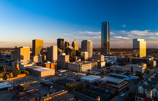 Downtown Oklahoma City skyline aerial during the golden hour, with late sun reflections on windows and a blue sky with some clouds in the background.