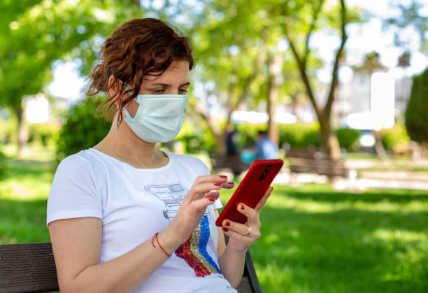istock Young woman in protective mask using smartphone in public park 1338527947