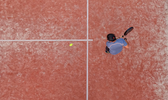 Top view of a padel player who is going to hit the ball with the racket during a padel match or practice on an outdoor court