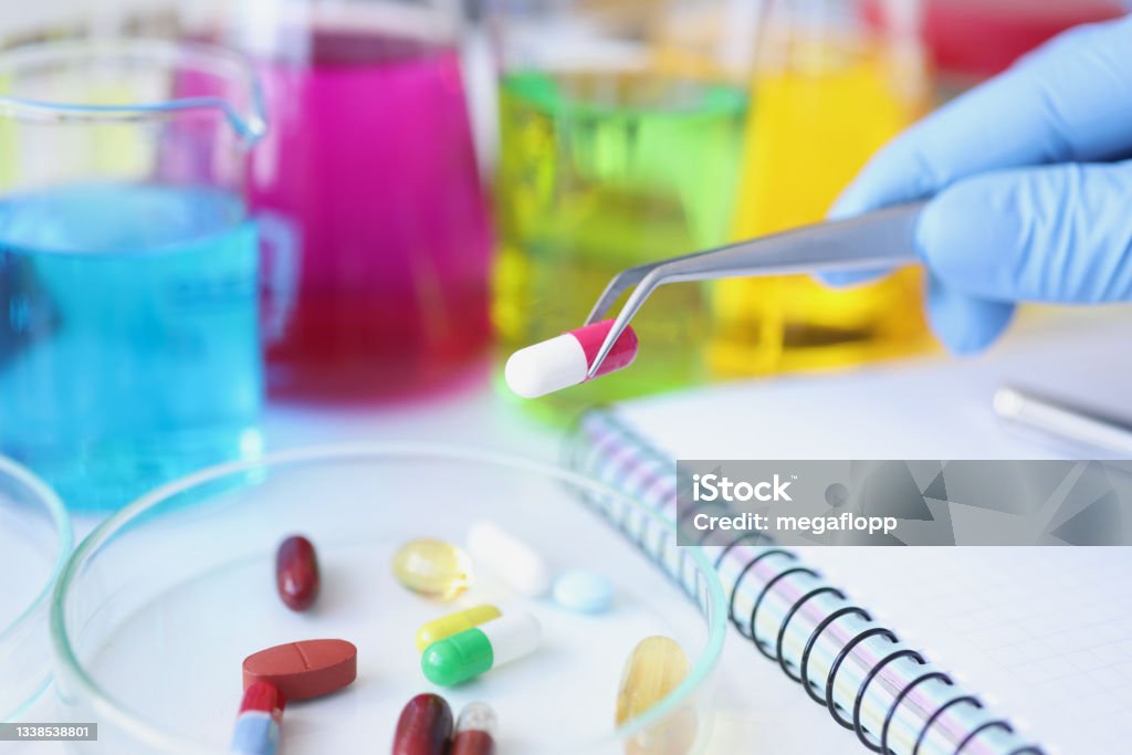 Scientist holds medical pill in forceps in laboratory closeup Scientist holds medical pill in forceps in laboratory. Drug development concept Rebellion Stock Photo