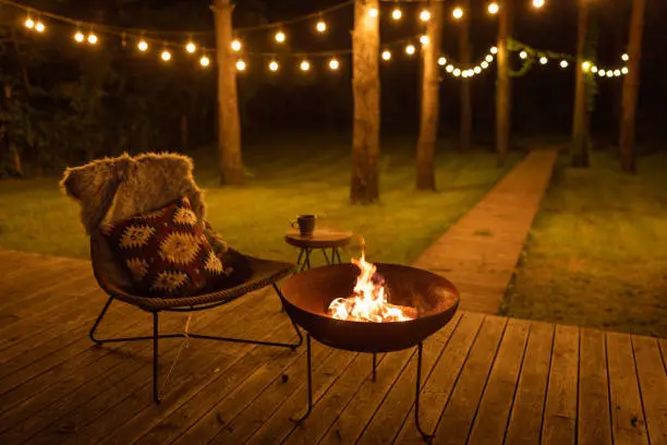 Comfortable arranged porch with fire pit and chairs. Autumn theme details. String lights in the background.