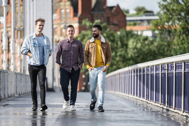 Men enjoying sunny weekend walk across Chelsea Bridge Full length front view of Caucasian and Indian male friends in casual clothing walking together in breezy weather after summer rain shower. approaching stock pictures, royalty-free photos & images