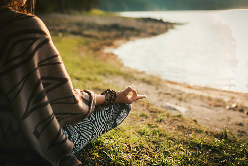 Young woman meditating near a mountain lake during sunset.