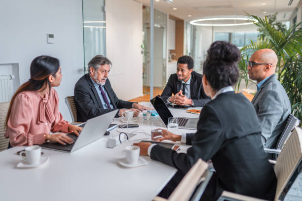 istock Multi-ethnic Group Of Businesspeople Conversing at Conference Table Before Meeting 1338554596