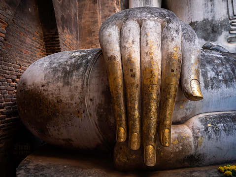 Close up hand of ancient buddha statue inside the church at Wat Sri Chum Temple, the famous landmark in at Sukhothai Historical Park, a UNESCO World Heritage Site in Thailand.