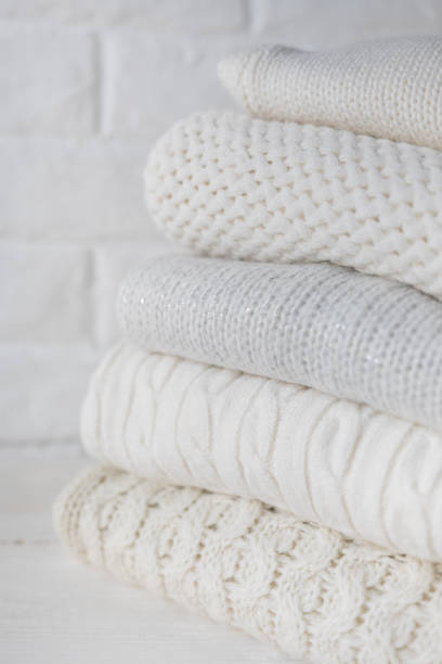 istock Stack of white cozy knitted sweaters and beads against the background of white brick wall. 1338590272