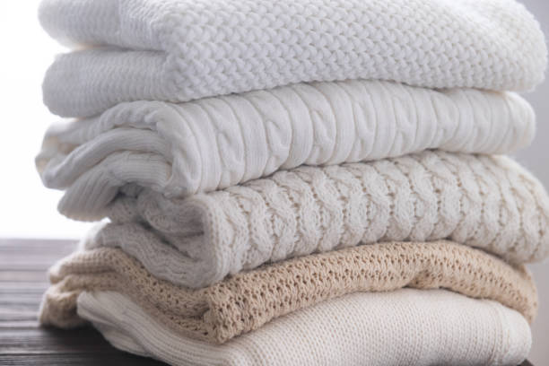 istock Stack of white cozy knitted sweaters on wooden table 1338590452