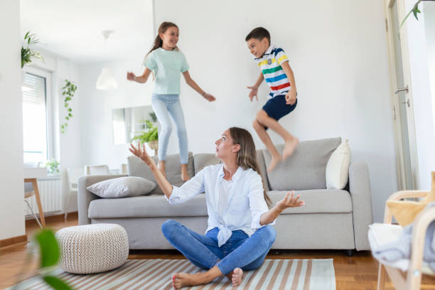 istock Tired young mother sitting on sofa and working with laptop and documents while little kids having fun and making noise 1338597257