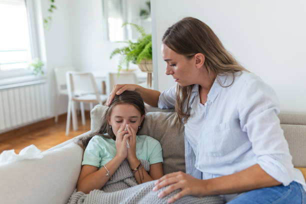 jovem verificando temperatura com a mão da filha doente. mãe verificando a temperatura de sua menina doente. criança doente deitada na cama debaixo do cobertor com mulher verificando febre na testa à mão. - daughter distraught little girls worried - fotografias e filmes do acervo