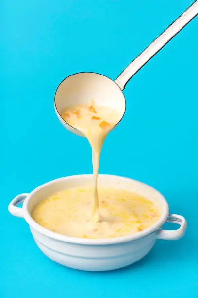 Delicious greek soup in white enamel bowl isolated on a blue background. Pouring soup from an enamel ladle into the bowl.