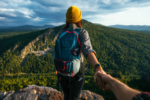Portrait of a woman holding her man's hand while walking along a mountain range. The couple is enjoying a walk in nature. A guy holds his girlfriend's hand in the mountains. A trip to the mountains stock photo