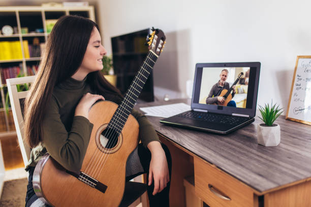 istock Girl playing guitar with computer, learn to play with an online course 1338602054